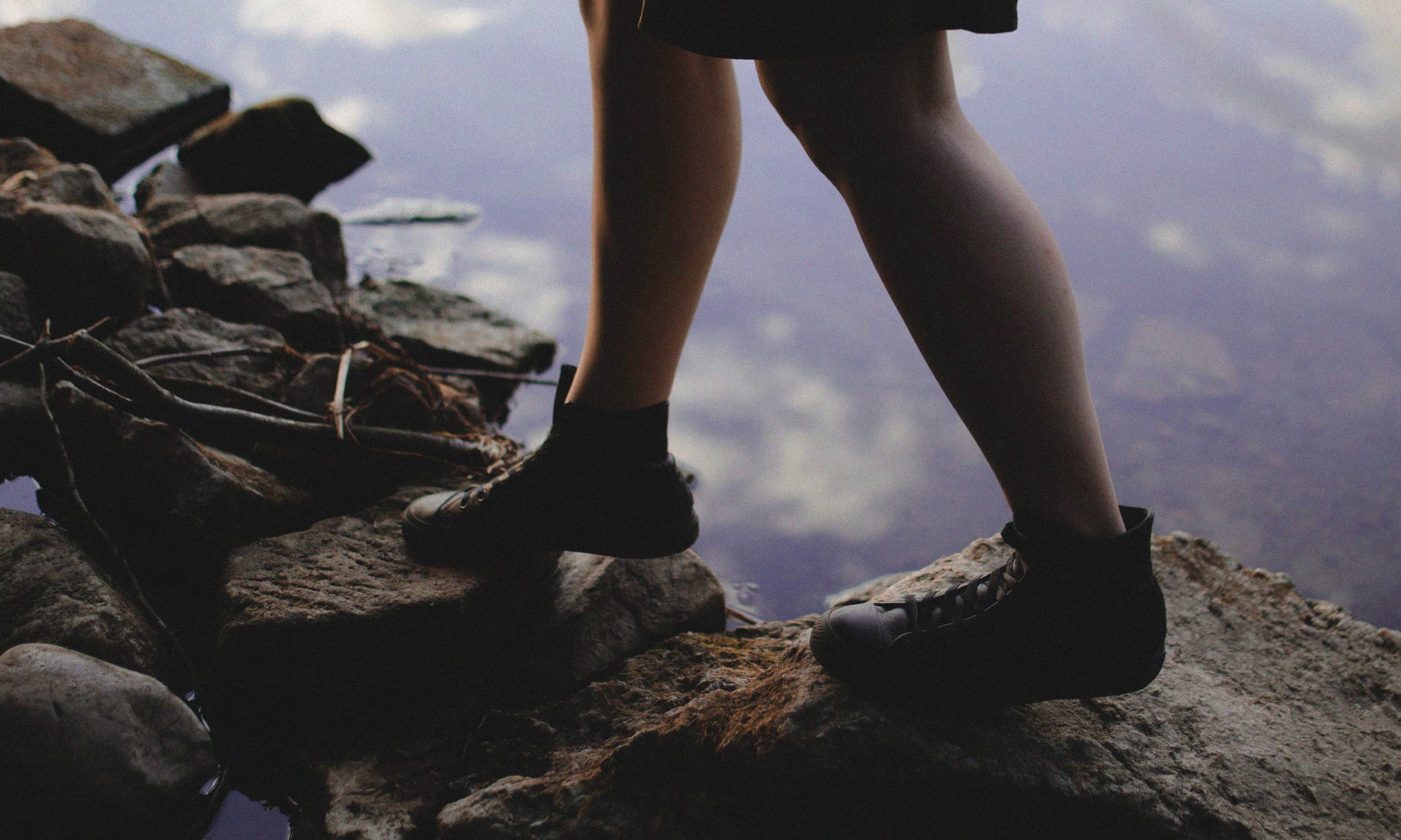 Person stepping across rocks beside calm water, symbolising what it means to feel emotionally grounded
