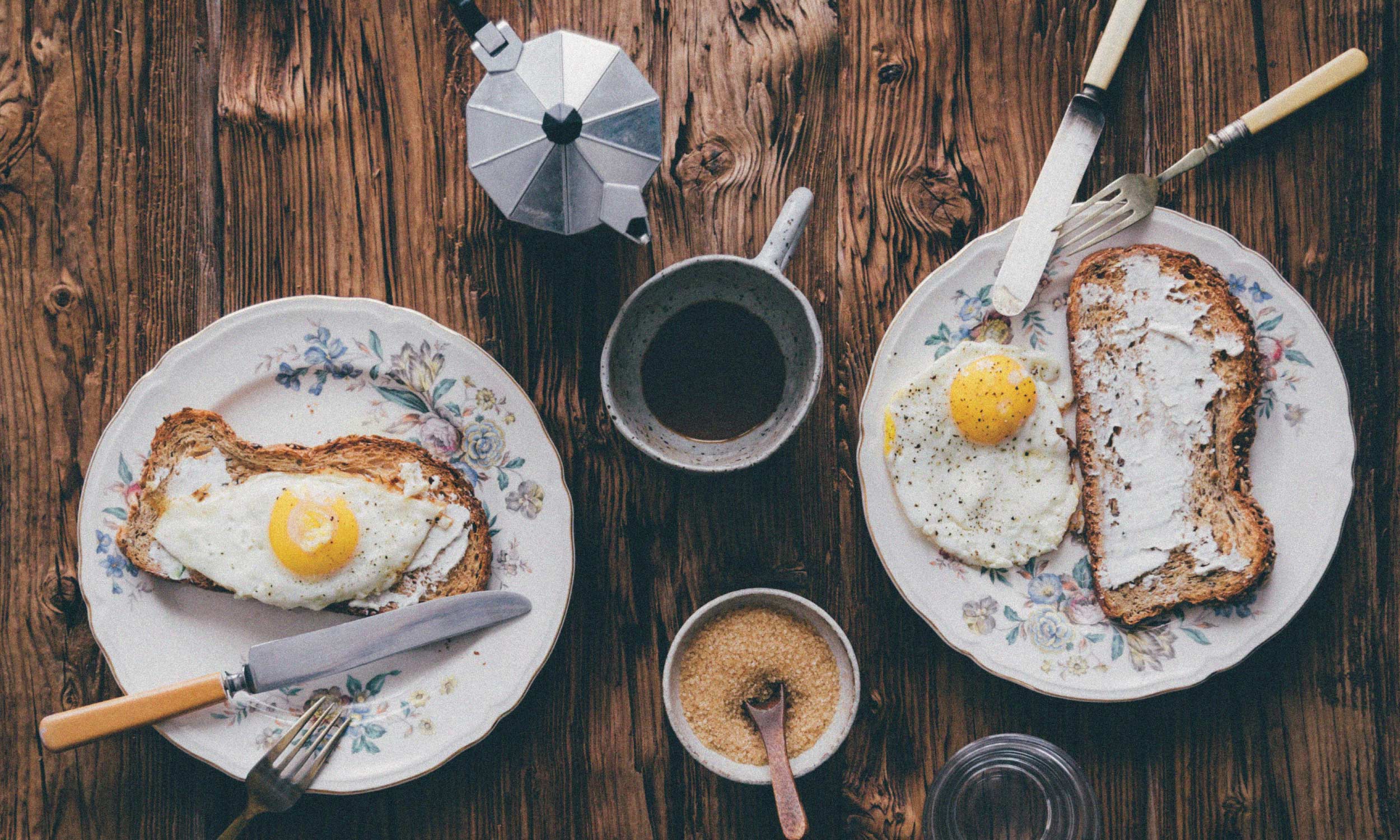 Overhead view of a high-energy, nutrient-rich breakfast with eggs on toast and coffee on a rustic wooden table
