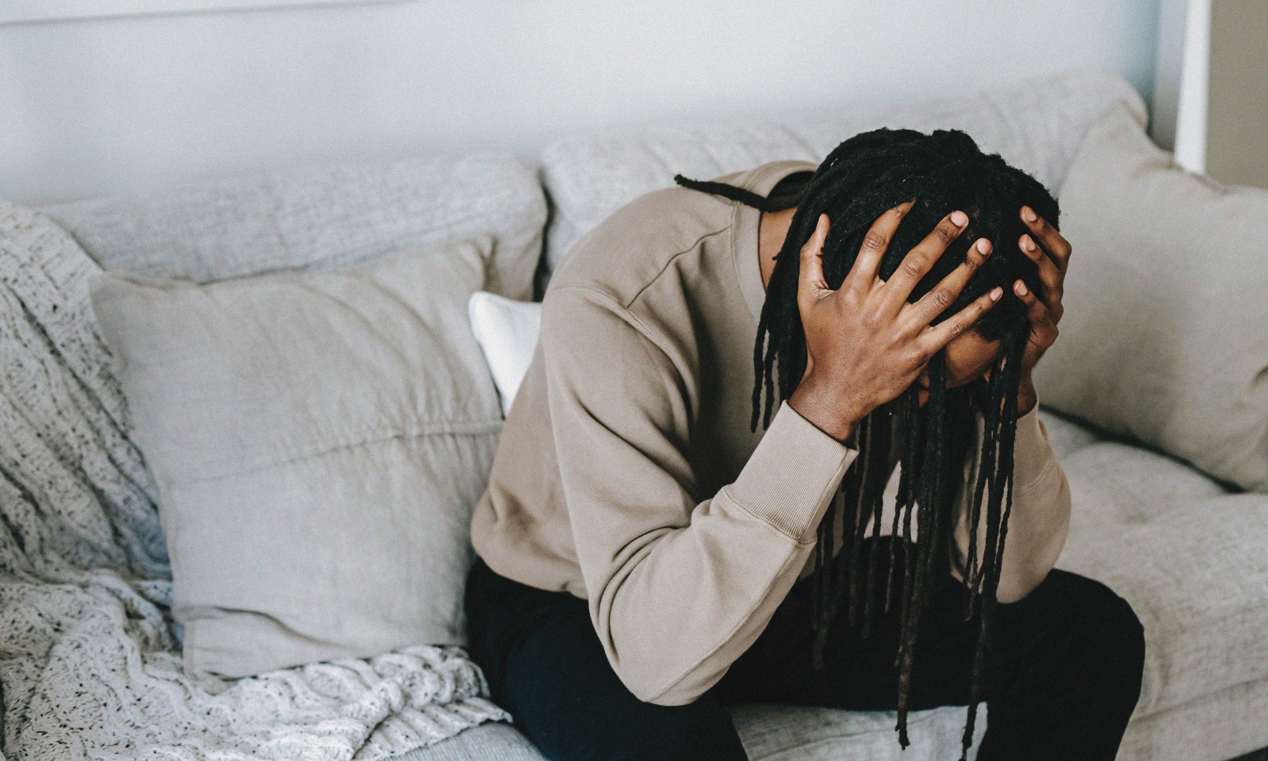Person sitting on a couch holding their head, illustrating how stress affects energy and causes emotional exhaustion