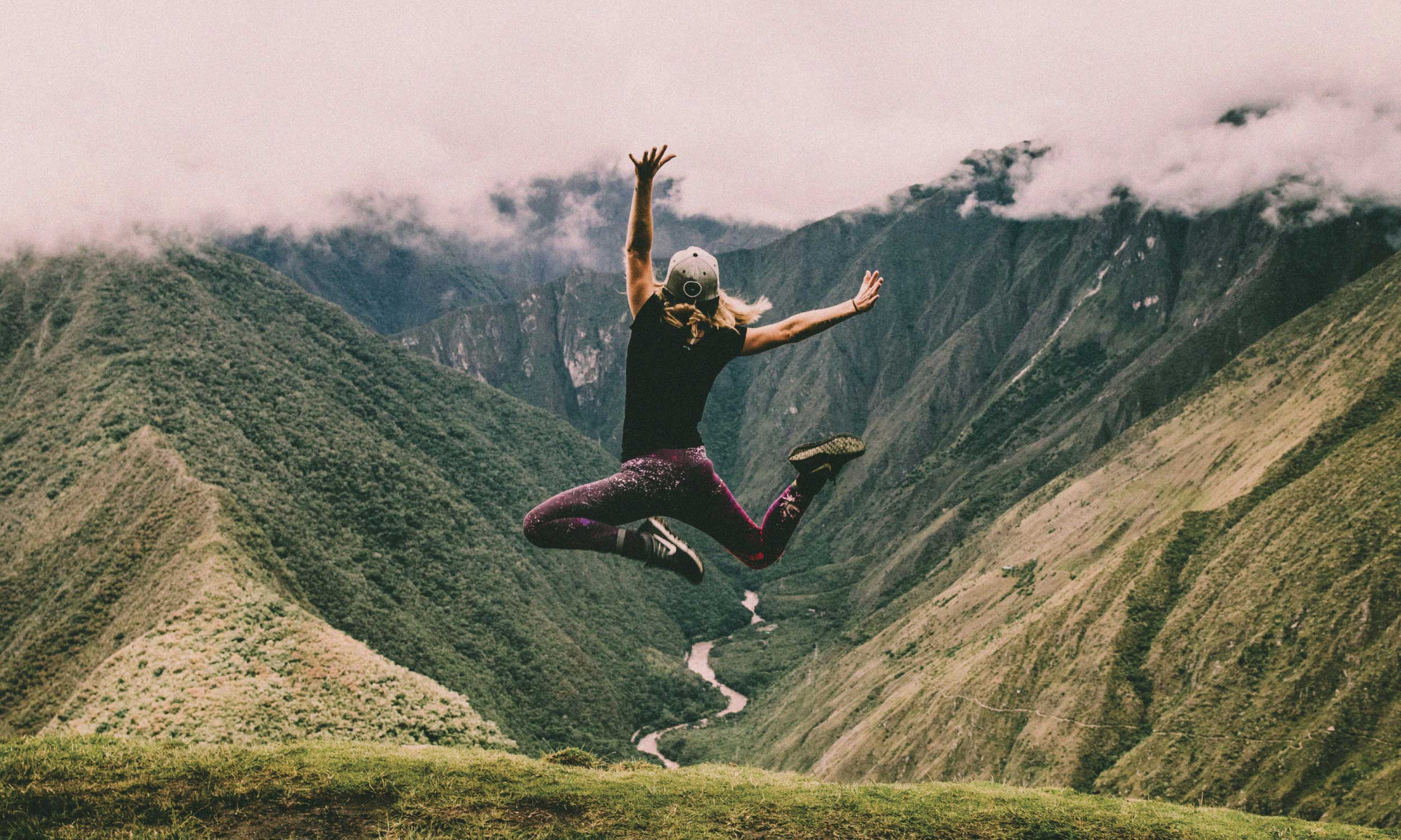 Woman jumping joyfully above a mountain valley, symbolising the energy to build a fulfilling life.
