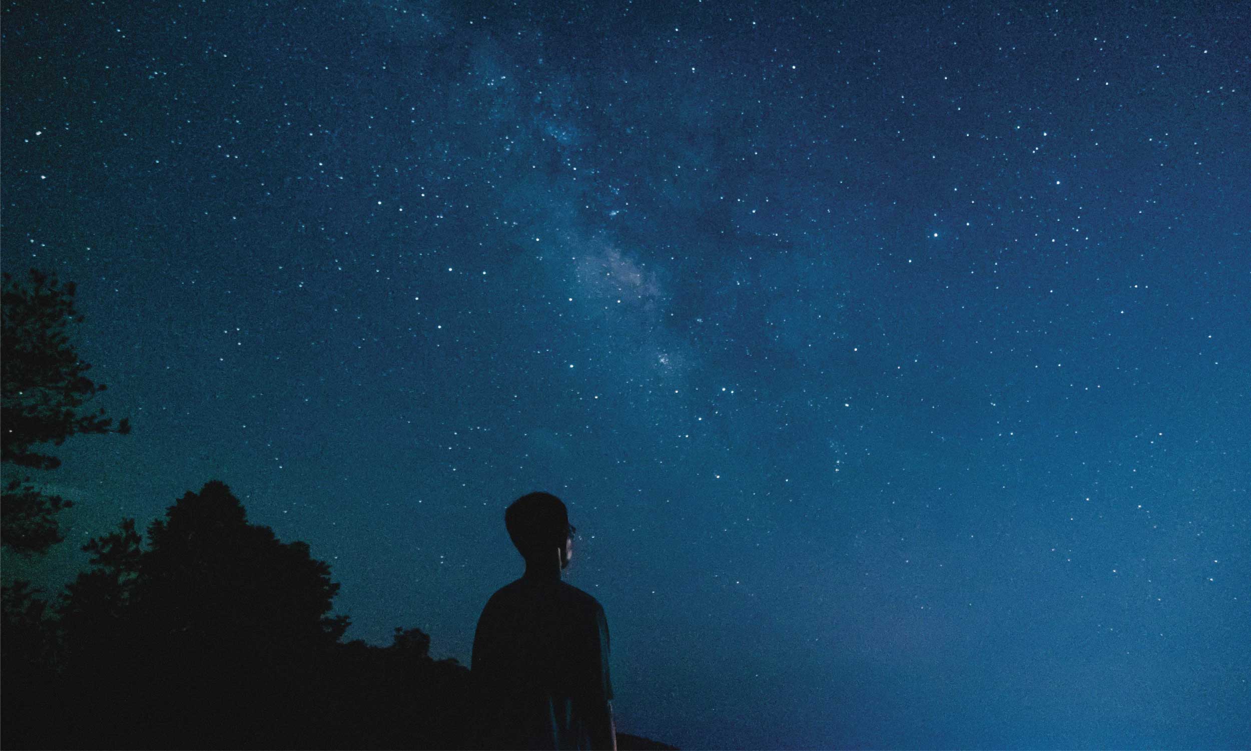 Person gazing at a star-filled night sky, symbolising how meaning shapes energy beyond daily habits.