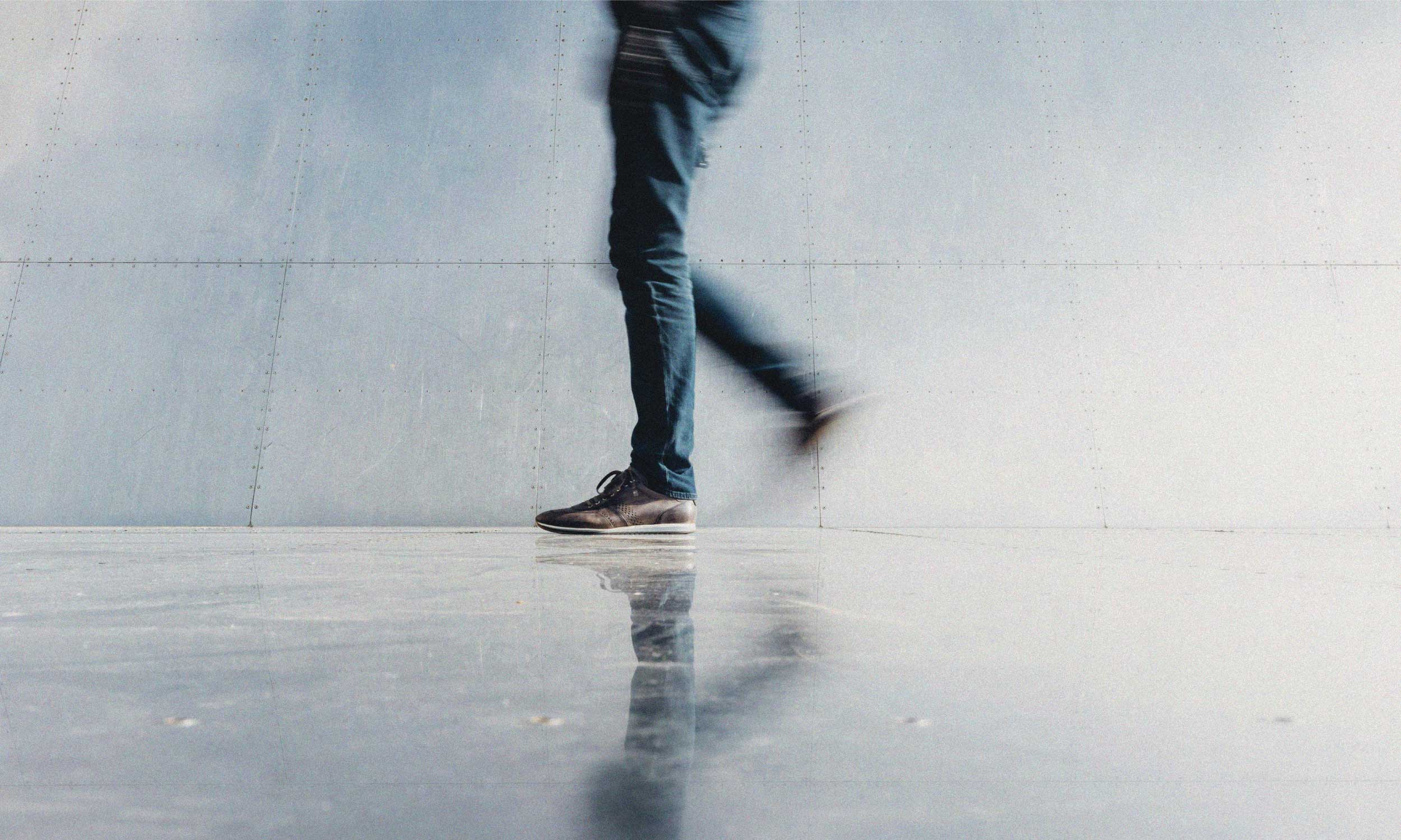 Person walking past a reflective wall, symbolising a new way of moving through the world.