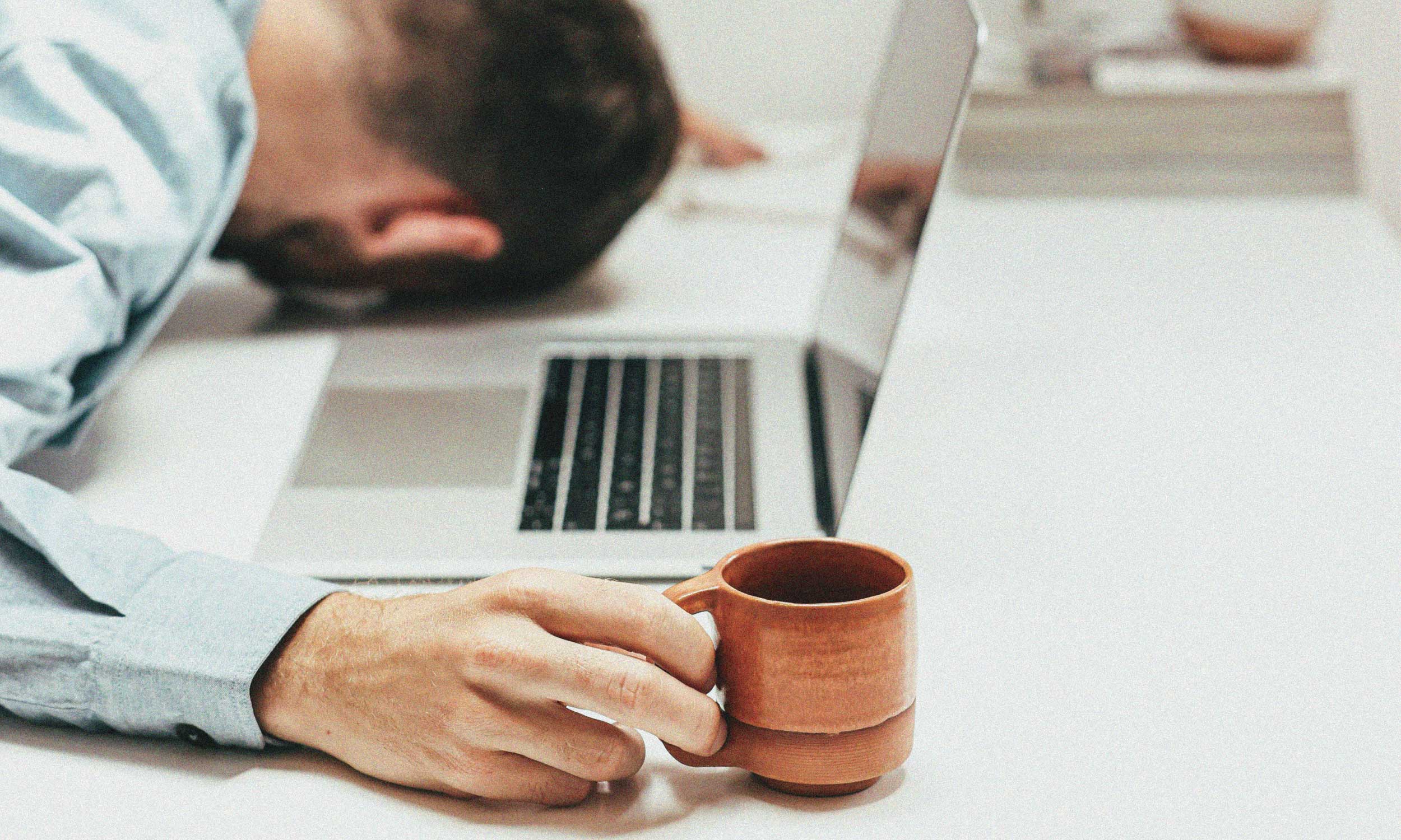 Person resting beside a laptop and coffee mug, reflecting on whether boredom is good for you.