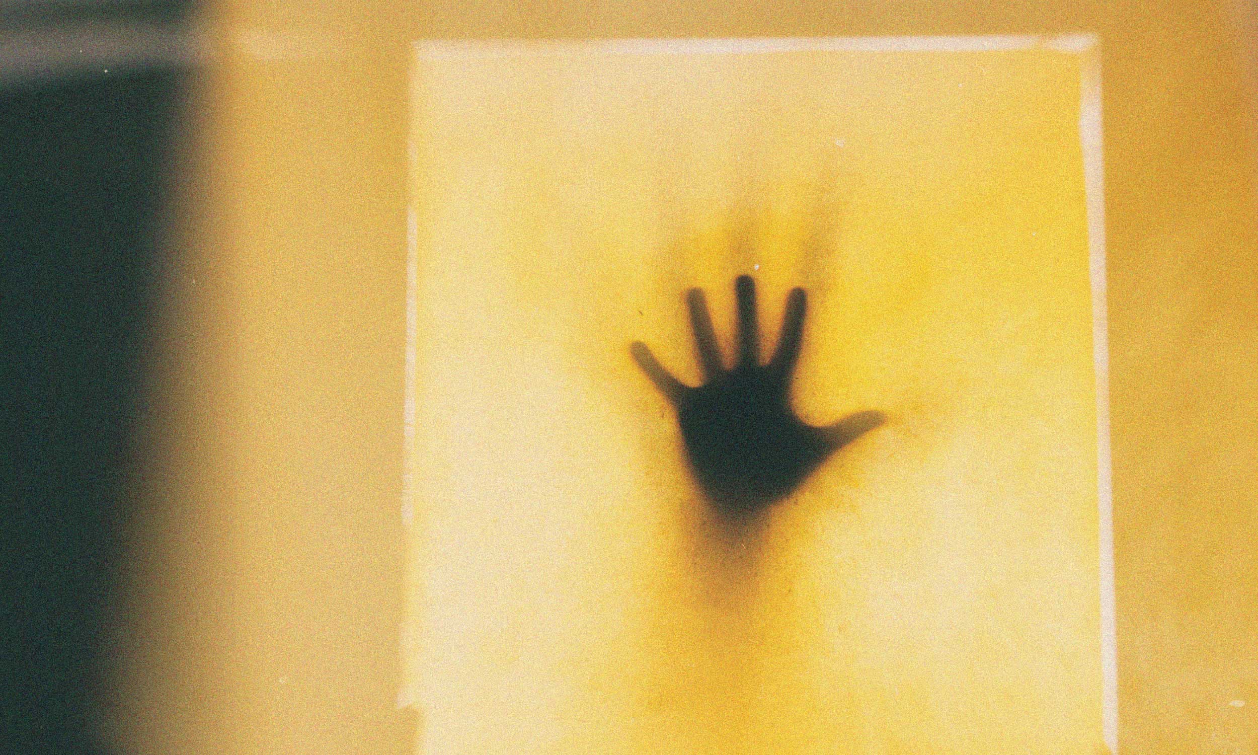 Silhouette of a person pressing a hand against frosted glass, symbolising fear disguised as control